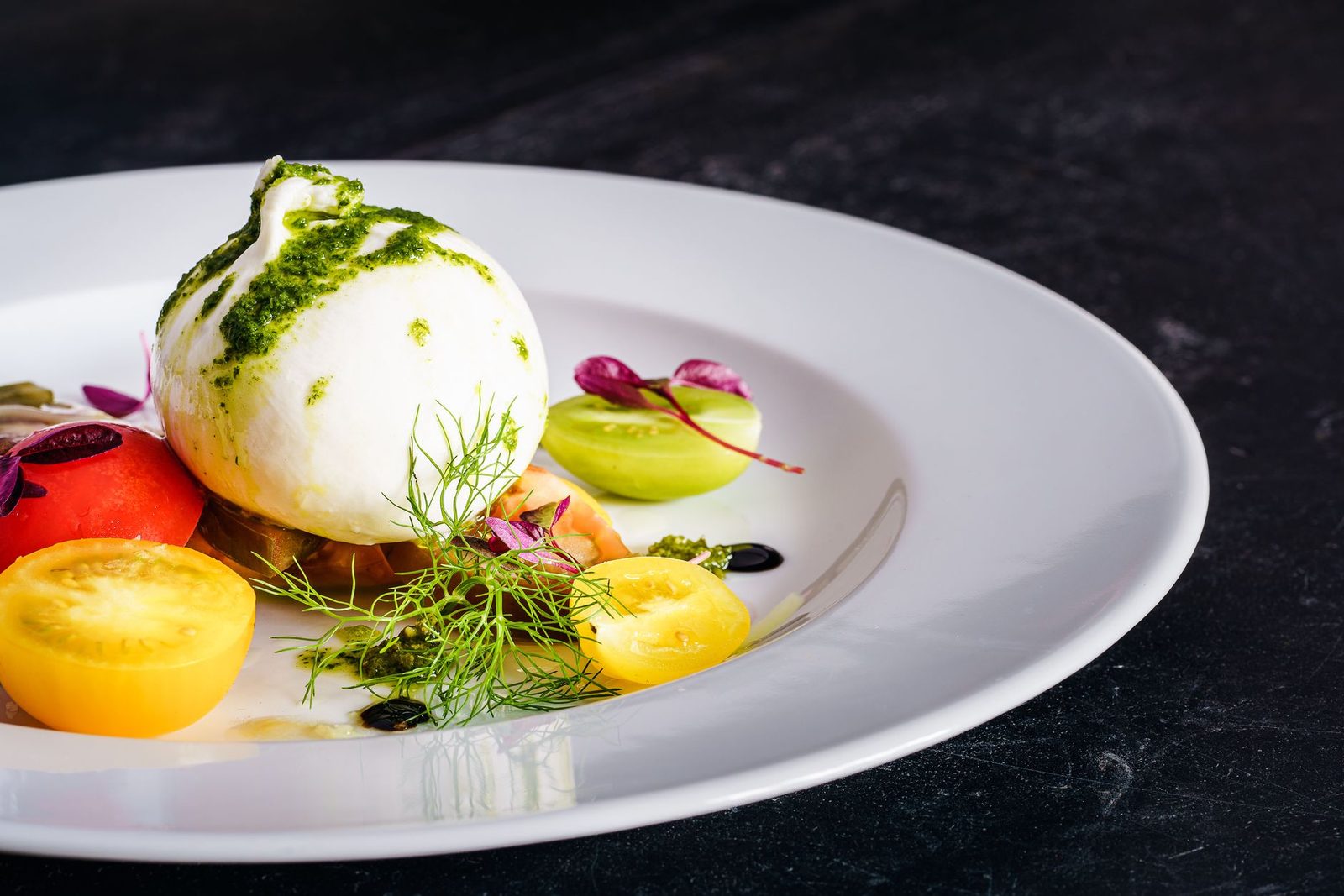 Burrata mit bunten Tomaten und Pesto auf weissem Teller